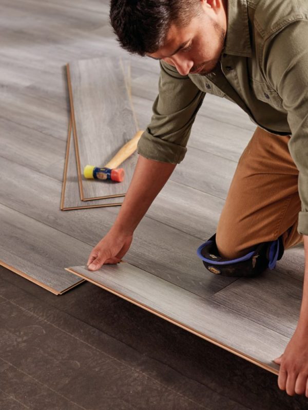 A man positioned on the floor, installing wood planks, illustrating flooring services in Las Vegas, NV.