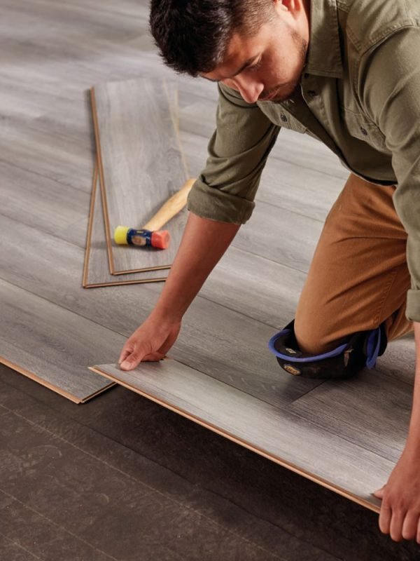 A man positioned on the floor, installing wood planks, illustrating flooring services in Las Vegas, NV.